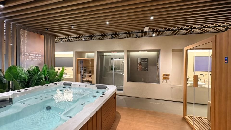 Technology, wellness & design. A spa pool in the foreground, with steam and sauna cabins and shower niches beyond, under a timber-slat ceiling.