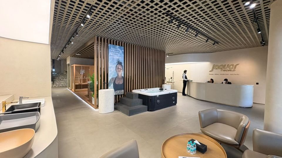 Reception. A curved reception desk with Jaquar World signage, lounge seating, a spa display and a slatted timber screen.