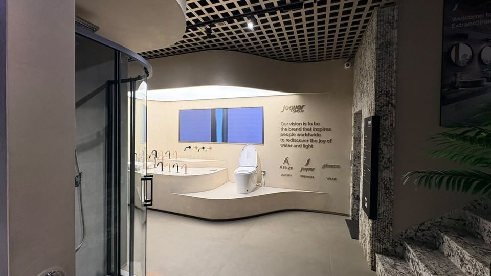 Brand vision wall. A curved plinth with basins and a smart toilet, below the brand-vision wall bearing the Artize, Jaquar and Essco marks.