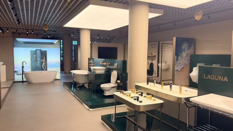 Laguna & freestanding baths. Freestanding and clawfoot baths on deep-green plinths, with a backlit shower image and gold basin stands.