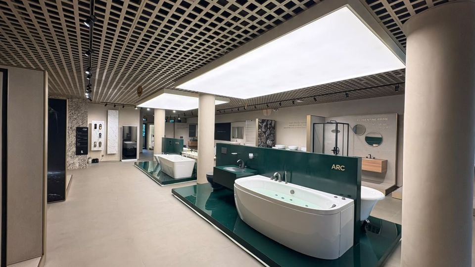 Arc whirlpool bath. A whirlpool bath on a green plinth before an Arc-branded partition, under a backlit ceiling panel.