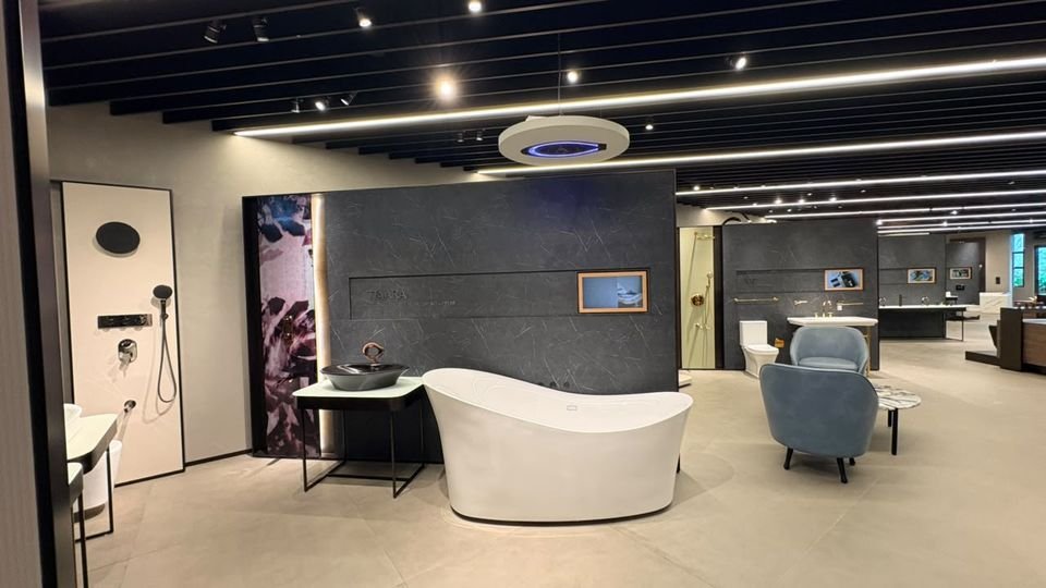 Bath, basin & lounge chair. A freestanding bath, a vessel basin on a black frame and an upholstered chair beneath an illuminated ring shower.
